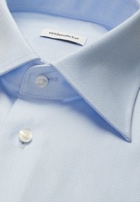 Lyseblå skjorte med spids krave, to hvide knapper og et synligt "seidensticker" mærke indeni kraven.