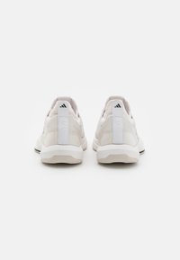 Zapatillas de entrenamiento de color claro con un material texturizado, detalles de tela suave y una pestaña en el talón blanca con el texto "TRAINING" en relieve.