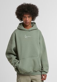 Olive green hoodie made of cotton blend, featuring a front pocket, drawstring hood, and white handwritten logo on the chest.
