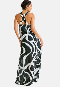 Robe maxi noir et blanc avec des motifs abstraits en spirale, col halter avec des bretelles croisées et un tissu fluide et léger.