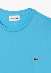 Camiseta azul claro hecha de 100% algodón Pima, con cuello redondo y logo de cocodrilo verde bordado en el lado izquierdo del pecho.