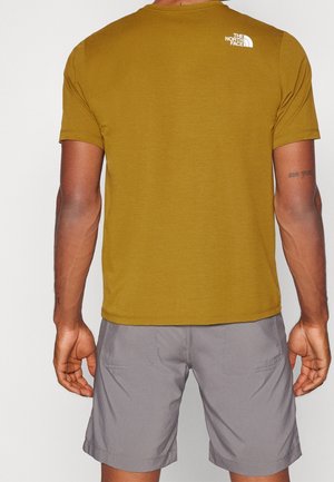 Mężczyzna w musztardowożółtej koszulce z krótkim rękawem z białym logo „The North Face” na górnej części pleców i jasnoszarych szortach, widziany od tyłu.