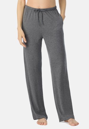 Frau trägt lockere graue Lounge-Hose mit Kordelzug in der Taille, steht barfuß vor einem schlichten Hintergrund.