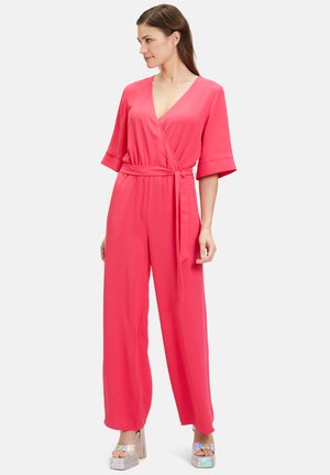 Pink wrap jumpsuit with short wide sleeves, a belted waist, and wide legs. Smooth texture and light fabric. Worn with shiny platform sandals.