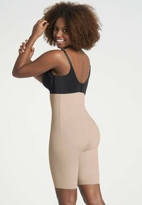 Beige shapewear bodysuit met een hoge taille en een lengte tot halverwege het bovenbeen, met een gladde textuur en naadloos ontwerp, gecombineerd met een zwarte bh.