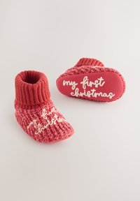Czerwone dziergane buciki z prążkowanym mankietem i teksturowanym panelem, z napisem „my first Christmas” w białym kolorze na podeszwie.