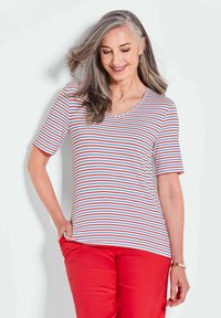Gestreiftes Kurzarm-T-Shirt in Weiß, Rot und Blau. Mit einem V-Ausschnitt und weichem Stoff. Kombiniert mit roten Hosen.