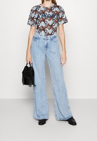 White and patterned t-shirt with “AMORE” text, paired with light blue wide-leg jeans. Accessorized with a black suede bag. Black footwear.