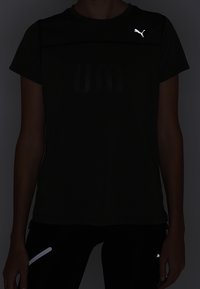 Svart tränings T-shirt med korta ärmar, med en reflekterande Puma-logotyp på höger axel och strukturerad väv med "UA"-mönster.