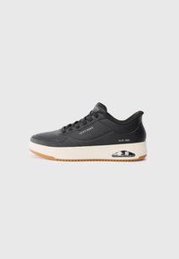 Black sneaker with a smooth finish, perforated design, and white midsole. Features gum outsole and visible air cushioning detail.