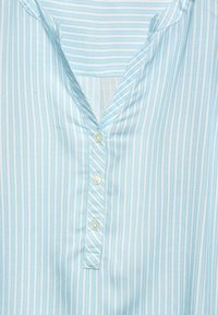 Camicia a righe blu chiaro con colletto a punte, patta con quattro bottoni bianchi e una consistenza di tessuto morbido e leggero.