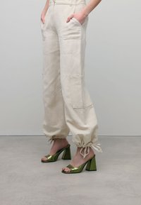 Beige linnenbroek met zijzakken en gather bij de enkels, gecombineerd met groene metallic blokhak sandalen met een open teen.