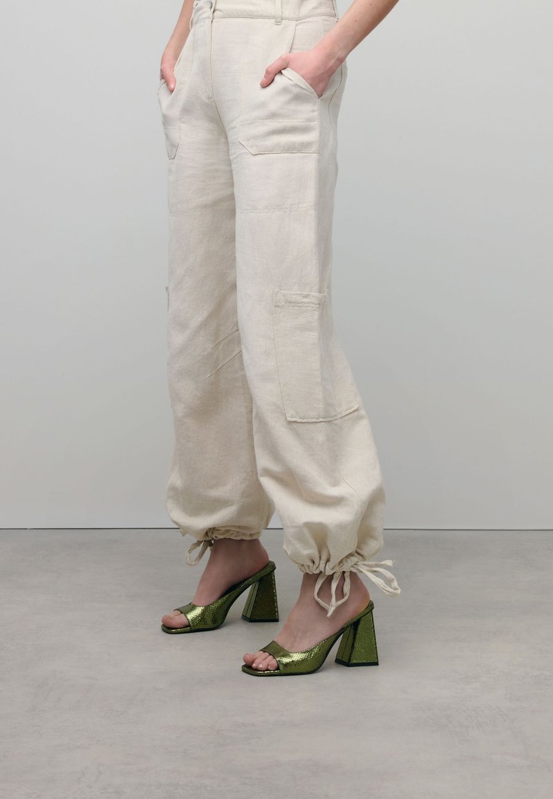 Beige linnenbroek met zijzakken en gather bij de enkels, gecombineerd met groene metallic blokhak sandalen met een open teen.