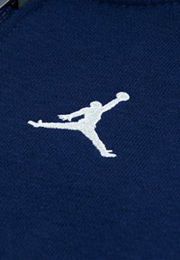 Tessuto navy con logo Jumpman ricamato in bianco, che mostra una silhouette in una posa dinamica, con una fine trama a maglia.