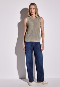 Ljusgrå stickad ärmlös topp med ett texturerat mönster, kombinerad med vida mörkblå jeans och beige sneakers. Ren bakgrund.