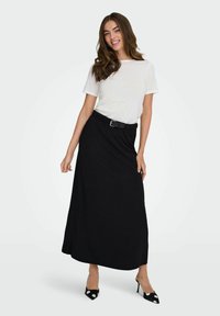 Jupe maxi noire avec une taille ajustée et une boucle argentée, associée à un T-shirt gris clair, en tissu doux et doté d'une silhouette fluide.