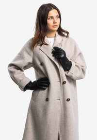 Light gray wool overcoat with a double-breasted design, large buttons, and side pockets. Worn with black leather gloves.