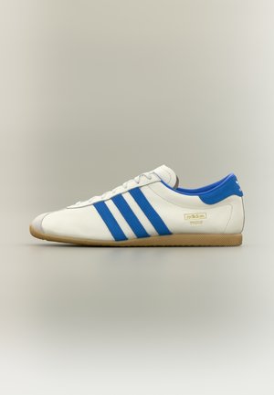 Biała skórzana tenisówka z niebieskimi akcentami, trzema niebieskimi paskami i gumową podeszwą. Posiada zaokrąglony nosek oraz branding "adidas Paris".