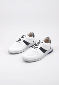 Des baskets blanches avec un design texturé, présentant des accents bleu marine foncé sur les côtés, des lacets noirs et une semelle en caoutchouc grise.