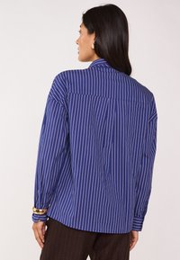Camicia blu navy con righe verticali bianche, dotata di un colletto strutturato e maniche lunghe. Tessuto testurizzato con vestibilità rilassata.