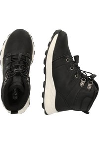 Bottes de randonnée noires avec une tige en cuir texturé, semelles en caoutchouc blanches contrastantes, et un design à lacets avec des œillets et des boucles en métal.