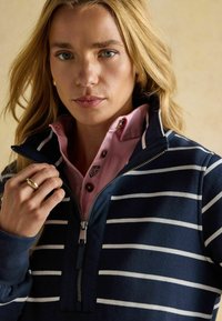 Tumedast triibuline pehme jakk, millel on lukuga krae, kantud heleda roosa särke, millel on nööbid. Kangas näib olevat pehme ja juhuslik disain.