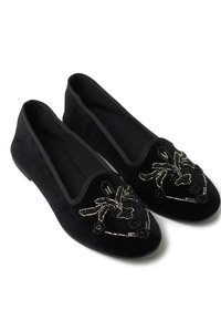 Los zapatos planos de terciopelo negro presentan una punta redondeada, bordes elásticos y cuentas decorativas en un diseño floral en la punta.