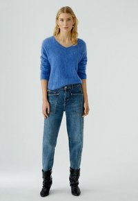 Hellblauer, flauschiger Pullover mit V-Ausschnitt, kombiniert mit ausgebleichten, lockeren Jeans im Cargo-Stil und schwarzen Stiefeln.