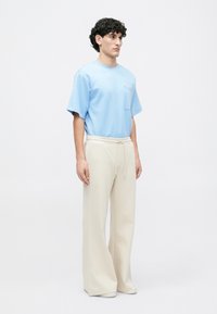 Camiseta de manga corta azul claro con un bolsillo en el pecho, combinada con pantalones de tiro alto y pierna ancha en color crema, que cuentan con una cinturilla con cordón.