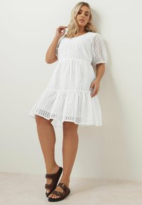 Vit bomullsklänning med texturerad öppen väv, puffärmar och utsvängd kjol. Parats med bruna sandaler med nitar.