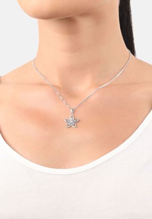 Collana d'argento con un pendente floreale con accenti a forma di petalo e una gemma centrale, montata su una sottile catena su uno sfondo di tono della pelle.