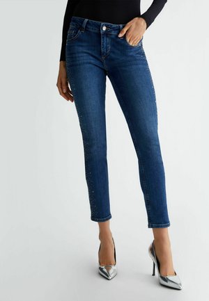 Jeans blu scuro con vestibilità slim, caratterizzati da strass decorativi lungo le cuciture laterali e un classico design a cinque tasche.