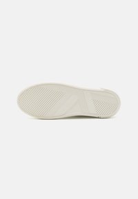 Sole di una sneaker in off-white, realizzata in gomma con un motivo a spina di pesce e dettagli testurizzati. Presenta un contorno liscio e arrotondato.