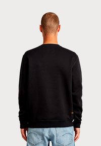 Felpa nera con collo rotondo e polsini a coste, con un'etichetta quadrata sul retro. Tessuto morbido con una texture liscia.