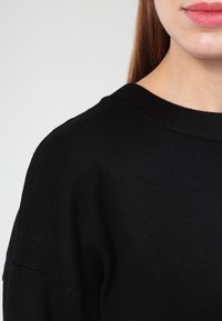 Zwarte gebreide trui met een ronde hals. Kenmerkt zich door een gestructureerde stof en een losse pasvorm, met ribgebreide details bij de kraag en manchetten.