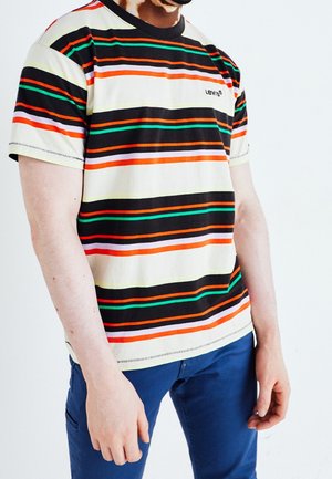 Homme portant un t-shirt Levi's à manches courtes avec des rayures horizontales noires, orange, vertes et blanches, associé à un pantalon bleu.