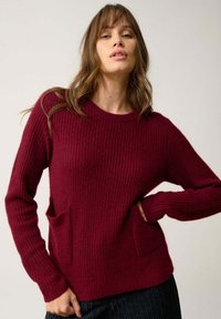Bordeaux ribbeltrui met lange mouwen en twee voorzakken, met een ronde halslijn en een losse pasvorm. Geweven stofdetail zichtbaar.