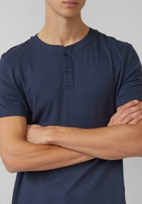 Marineblauw henley-shirt gemaakt van gestructureerde stof, met een ronde hals, drie knopen aan de voorkant en korte mouwen.