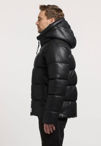 Giacca nera imbottita con colletto alto e cappuccio, caratterizzata da una texture liscia e lucida, tasche con zip e rifiniture elastiche sui polsini.