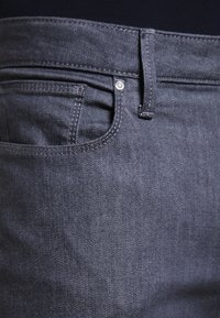 Mörkgrå denimjeans med en slät yta, utrustad med en framficka, bältesöglor och en liten metallnitar. 