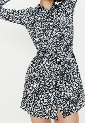 Zwarte bloemenjurk met witte bloemenpatronen, knoopsluiting, een kraaghalslijn en een riem met een ronde gesp in de taille.