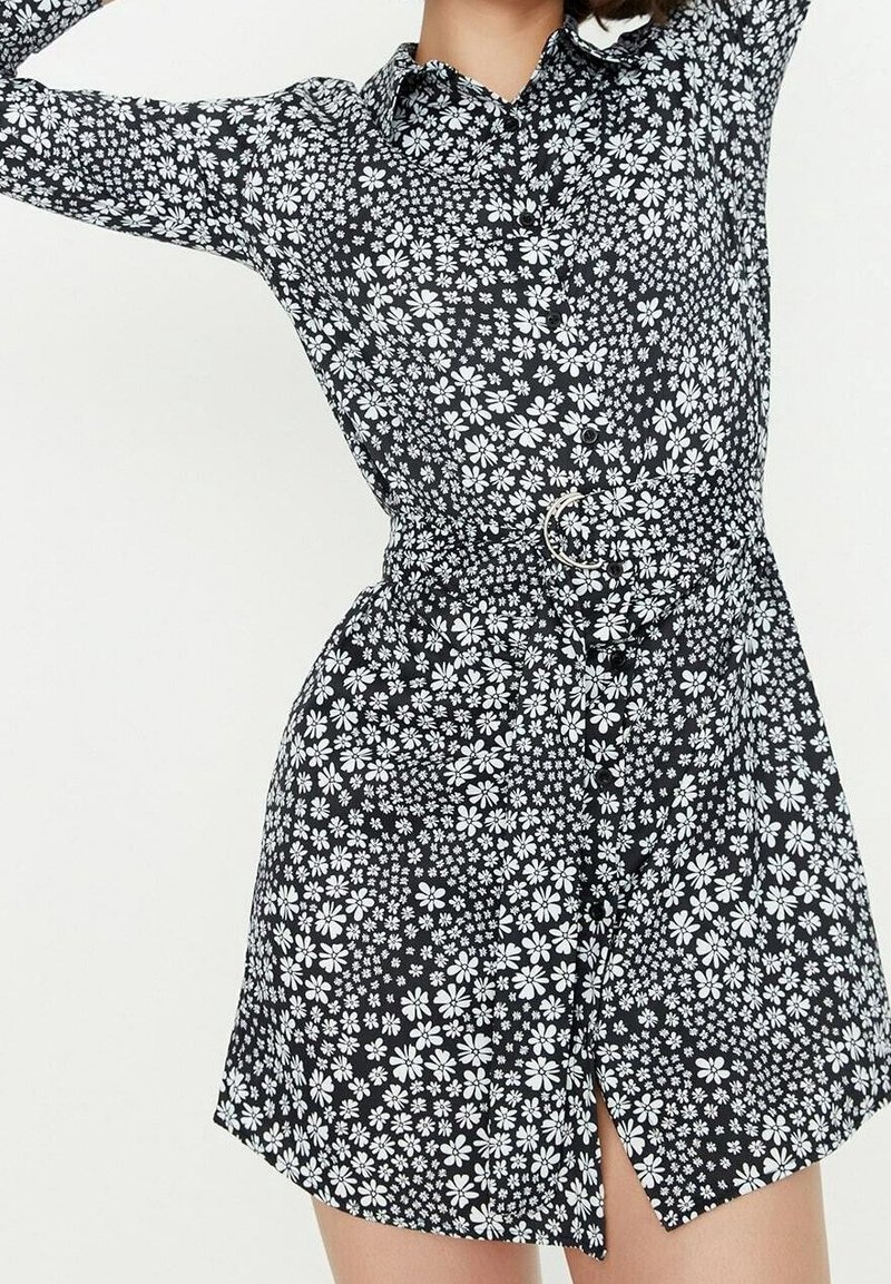 Schwarz geblümtes Hemdkleid mit weißen Blumenmustern, Knopfverschluss, Kragenhöhe und einem Gürtel mit rundem Schnallenverschluss in der Taille.