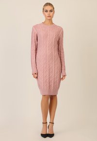 Sweter-dress z dzianiny w warkocze w delikatnym różu, z okrągłym dekoltem, długimi rękawami i ściągaczem na dole. Gładka faktura dzianiny i dopasowany krój.