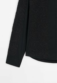 Chemise noire à manches longues avec broderie florale ton sur ton le long de la manche et sur le panneau latéral avant, dotée de manches à poignets et d'un ourlet arrondi.