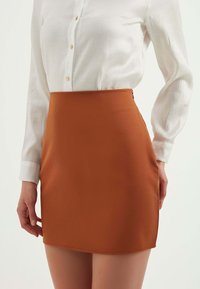 Bruine nauwsluitende rok met een zachte textuur en een zijrits, gecombineerd met een witte blouse met knopen en een subtiel verticaal patroon.