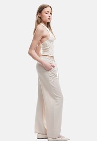 Beige kurzes Tanktop mit kleinen dekorativen Punkten, kombiniert mit lockeren, hellbeigen Hosen mit seitlichen Taschen und elastischem Bund.