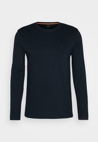 Camiseta de manga larga en color navy hecha de algodón, con un cuello redondo y un pequeño parche de logo en el pecho. Textura suave con una forma ajustada.