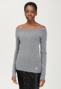Grijze off-shoulder trui gemaakt van zachte gebreide stof, met lange mouwen en een geribbelde zoom. Gepaard met een zwarte rok versierd met studs.