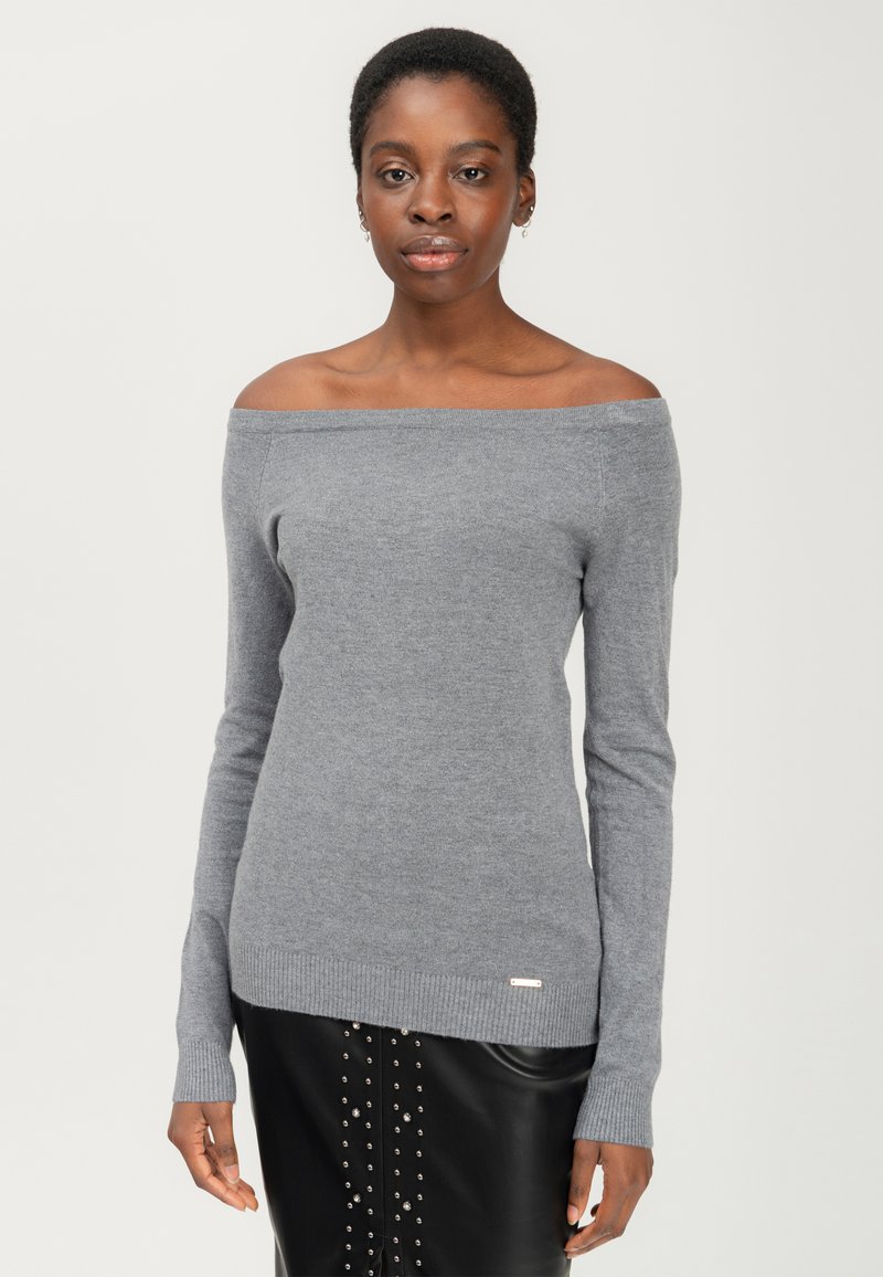 Grijze off-shoulder trui gemaakt van zachte gebreide stof, met lange mouwen en een geribbelde zoom. Gepaard met een zwarte rok versierd met studs.