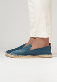 Espadrilles bleues en suede avec une semelle en corde de jute, présentant une texture lisse et un design à côté découpé. Chaussures décontractées adaptées aux temps chauds.